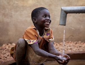 A child plays in clean water from a new handpump in Zambia [WaterAid/ Anna Kari]