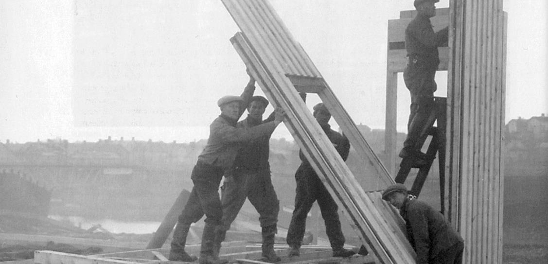 Workmen erect a Puutalo house on a site in Finland using pre-fabricated panels. These elements arrived from the factory with their exterior cladding already installed. Photo from 1940.
© ELKA