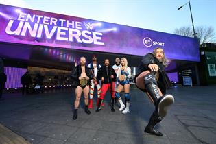 Five wrestlers stand on the walkway between Wembley Park Underground station and Wembley Stadium