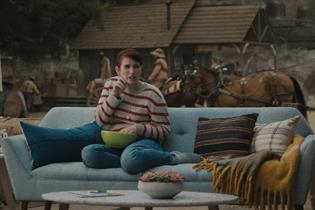 A woman sits on her sofa but in the background are the signifiers of the Wild West.