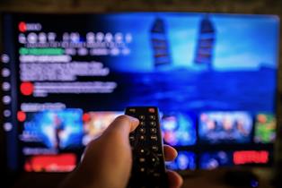 Someone pointing a remote controller at their smart TV, which is displaying an out-of-focus Netflix menu