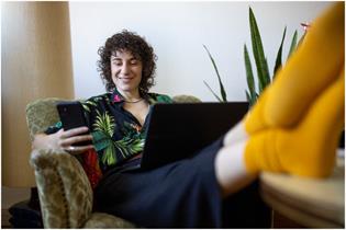 Person sitting with their feet up using a laptop and a mobile phone 