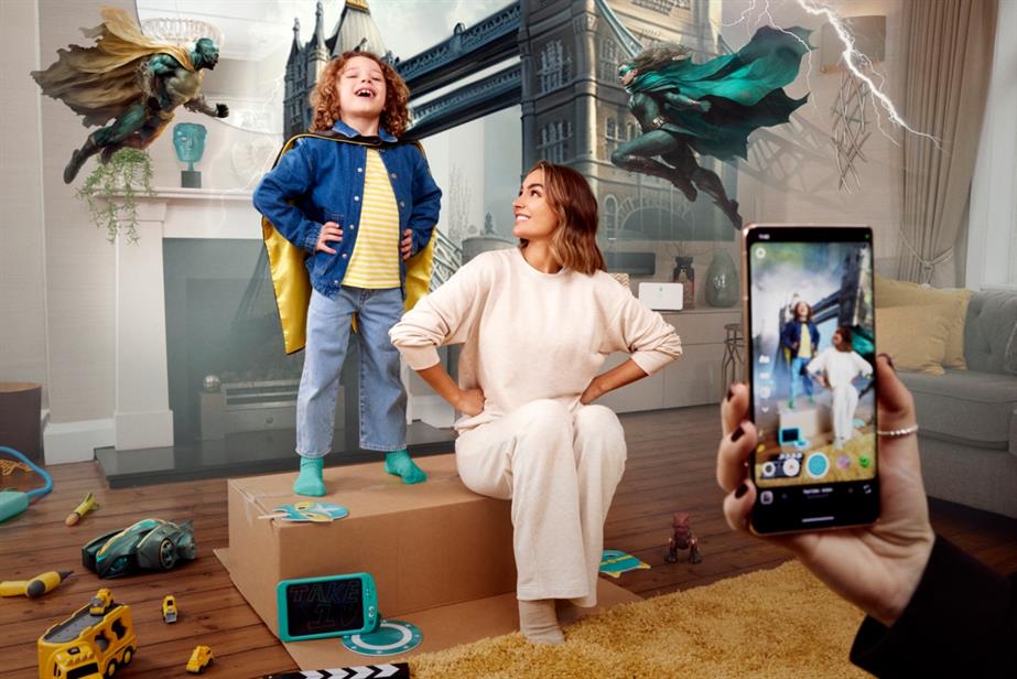 A mum and her son sit in the living room, with two action superheroes facing off behind them.