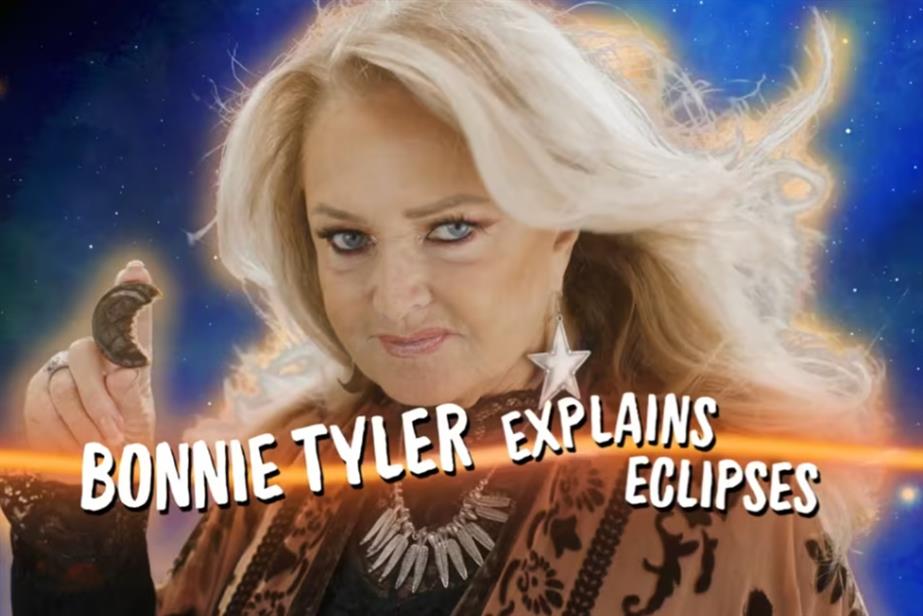 Bonnie Tyler stares at the screen with a Jaffa Cake in hand. The caption is "Bonnie Tyler explains eclipses"