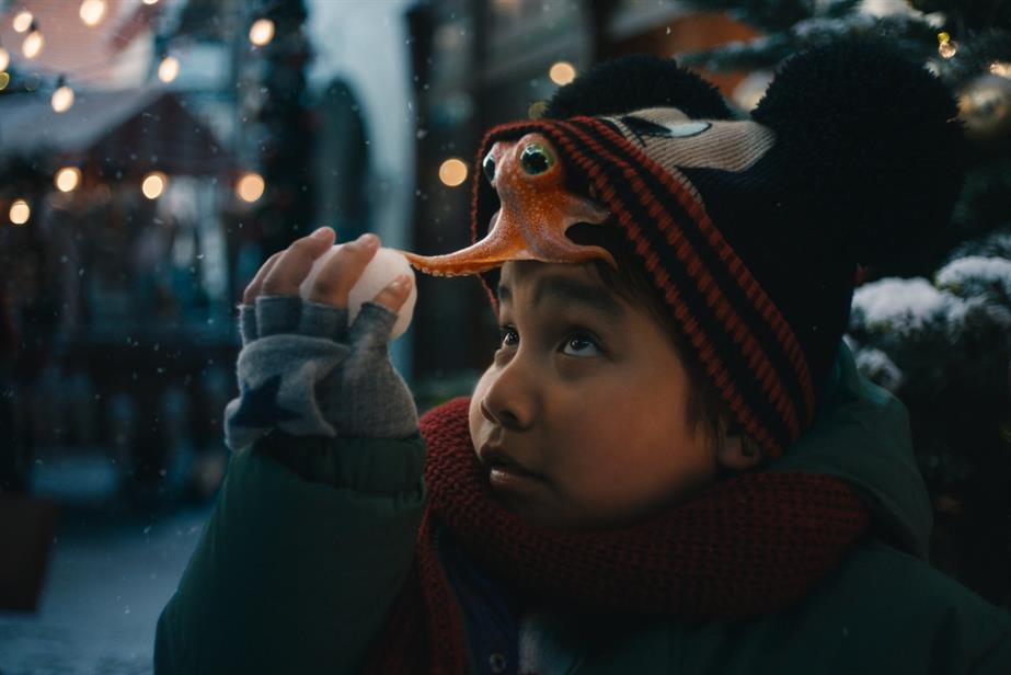 Young boy looks up at the octopus on his head, hidden under a Mickey Mouse hat, as the octopus touches a snowball.
