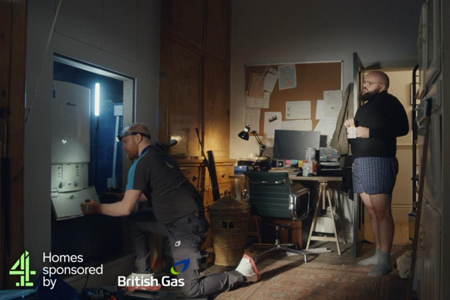 A man stands behind a British Gas engineer, observing him fitting his boiler.