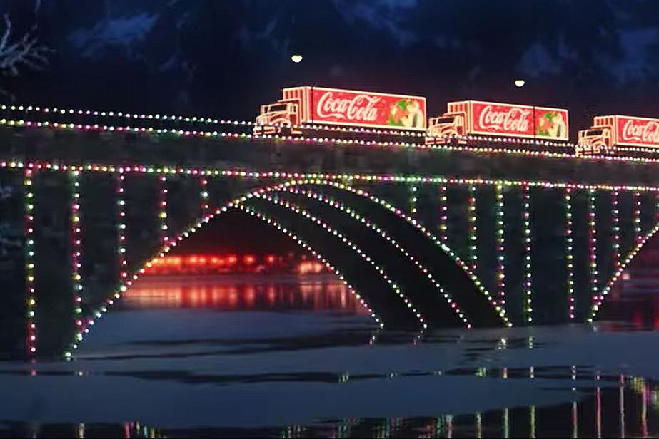 Brightly illuminated Coca-Cola trucks drive across a bridge lit up in multi-hued lights