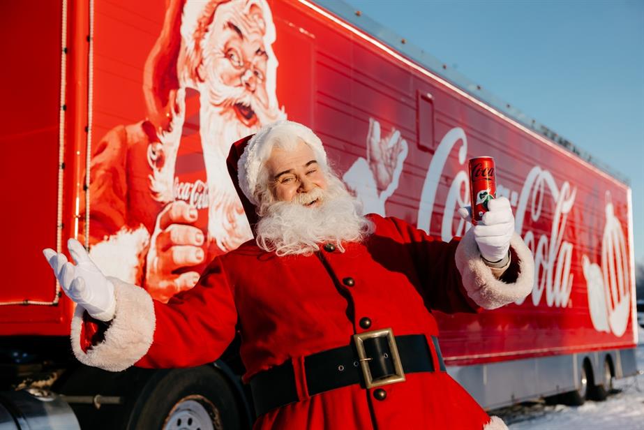 Santa stands in front of a Coca-Cola branded truck.