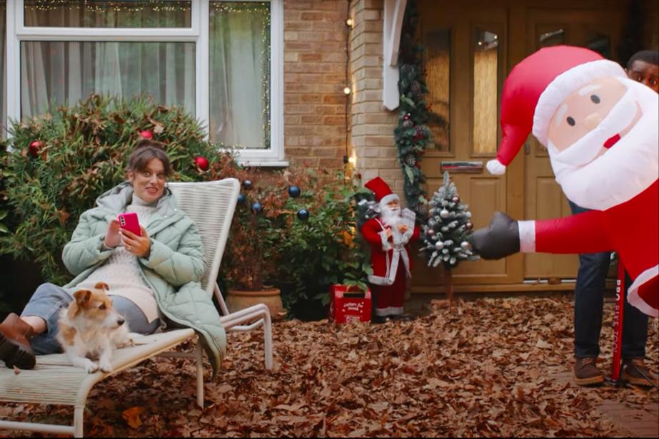 Woman sitting outside while man blows up inflatable Santa
