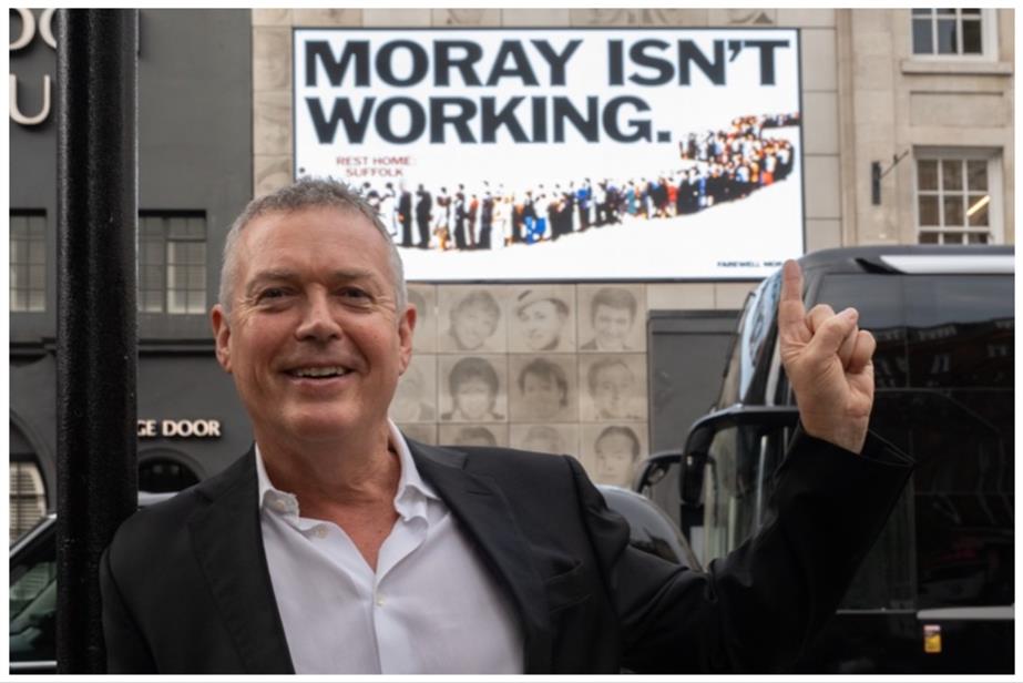 Moray MacLennan in front of a poster recreating Saatchi's "Labour isn't working" campaign