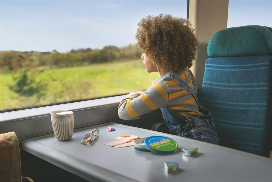 a kid on a train looking out at the UK countryside, on the table a circular box of Dairylea