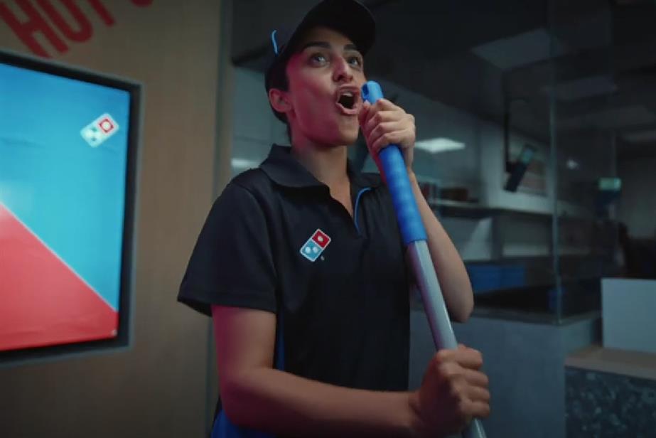 A female Domino's worker sings using her mop as a microphone prop