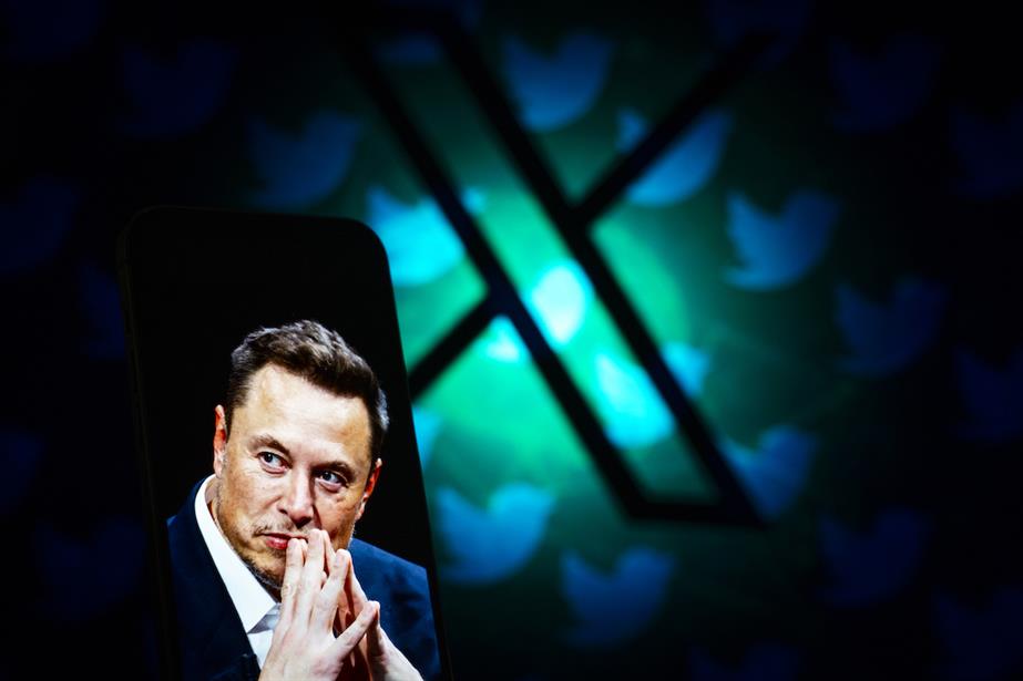 Elon Musk pictured on smartphone in front of giant backlit X logo