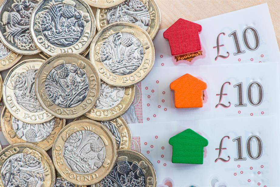 A pile of pound coins, a fan of £10 notes and some small wooden board game pieces in the shape of houses