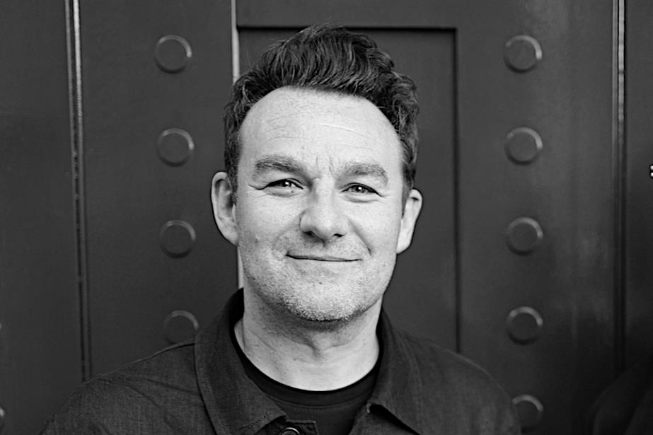 Black and white head and shoulders shot of James Morris in front of a door. Looking at the camera with a faint smile