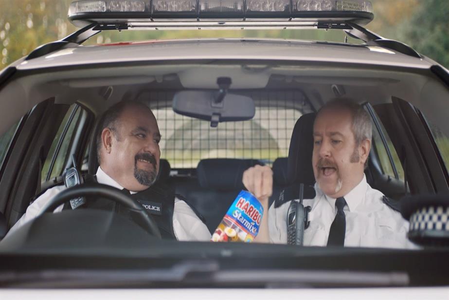 Image taken from a recent Haribo TV advert showing two policemen in a car sharing a bag of the sweets