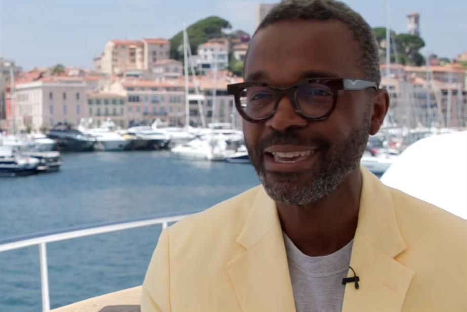 Lucien Etori, wearing a yellow jacket and stylish spectacles, is smiling, sat on a yacht in the harbour at Cannes