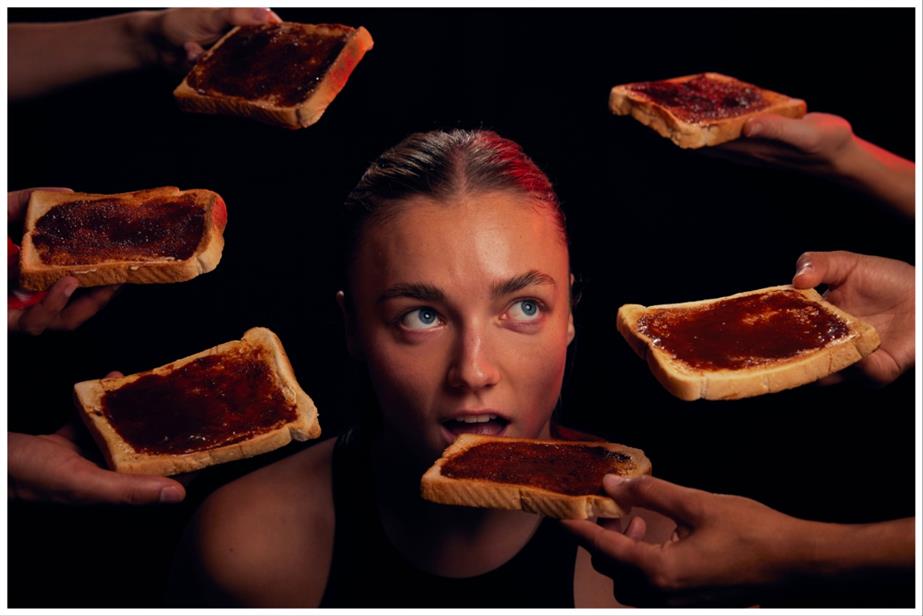 A woman with her mouth open to several slices of Marmite-covered toast