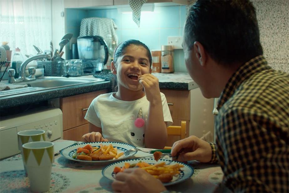 A young girl eats McCain ships at the dinner table with an older man