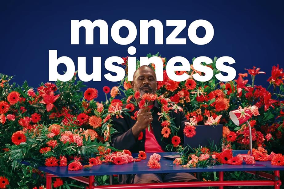Man sat at blue table surrounded by red flowers with 'Monzo business' written above his head