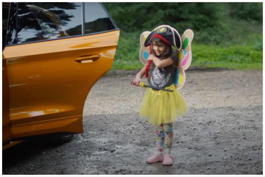 A young girl standing beside a car