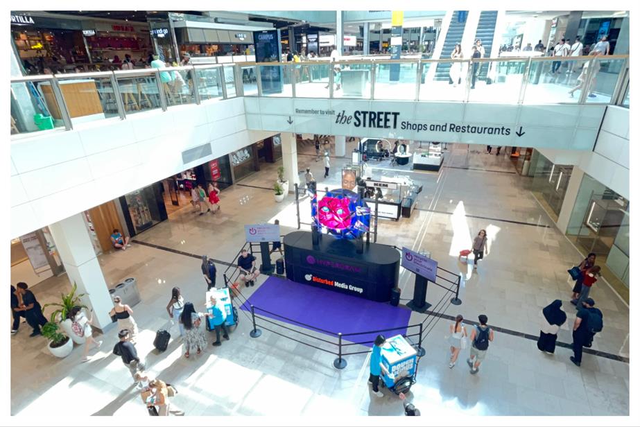 a stage with a giant pick cat hologram at a station full of commuters