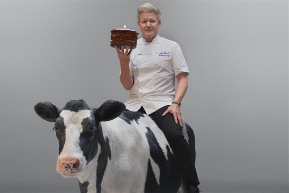 Gordon Ramsay sitting on a cow holding a cake