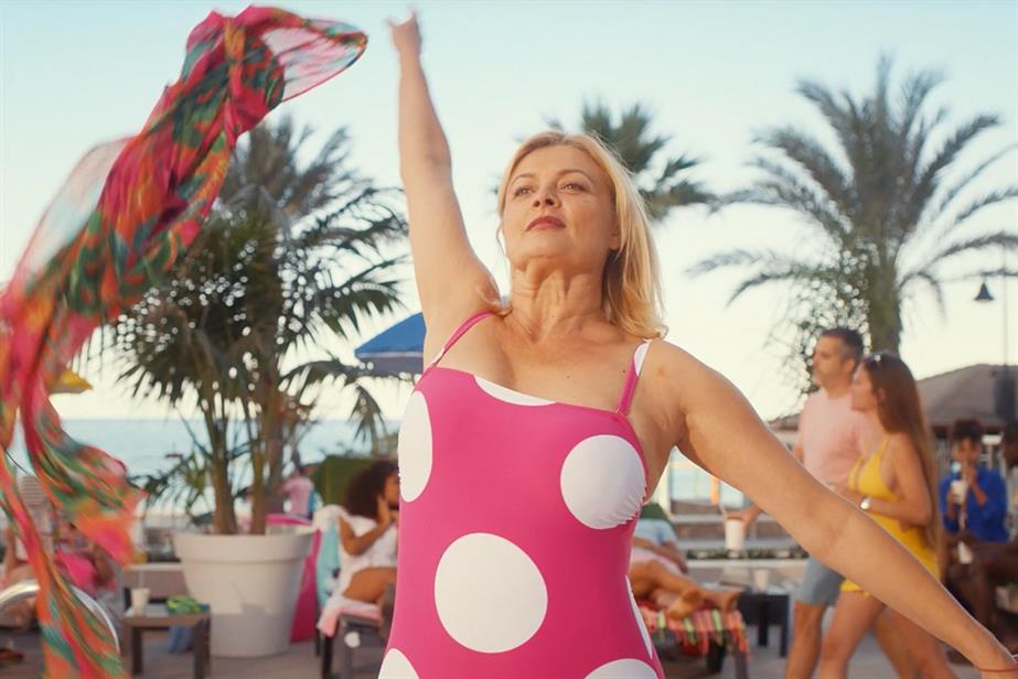 Still from On the Beach campaign, showing a woman in a pink swimsuit with white polka dots in a celebratory pose