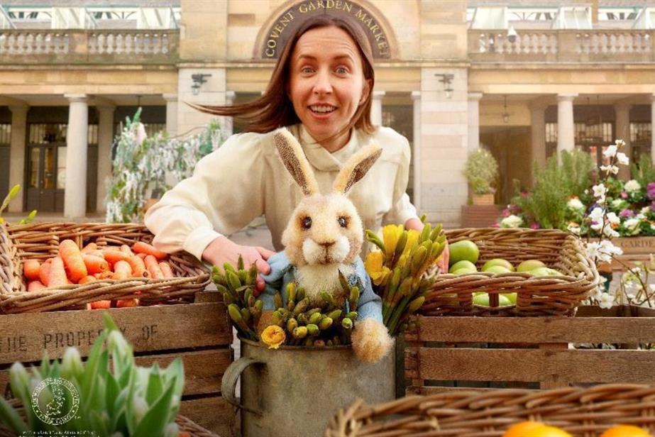 A woman in Covent Garden smiles at the camera with a Peter Rabbit puppet in front of her