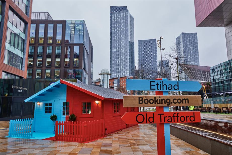 A half-red, half-blue house with road signs pointing towards Etihad Stadium, Old Trafford and Booking.com