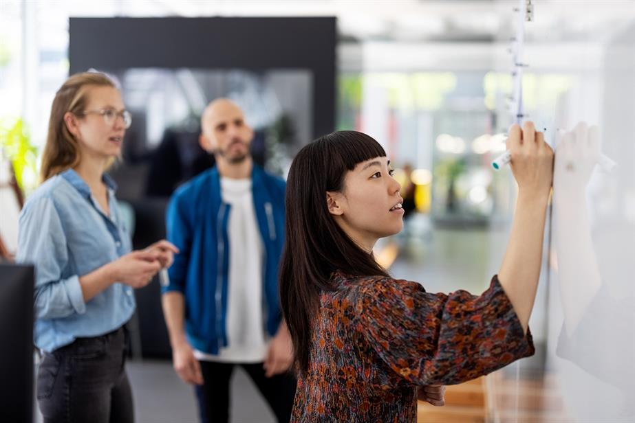 A lady writes on a whiteboard watched by colleagues. Photo: Getty Images
