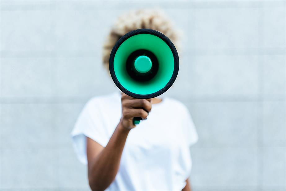 Woman with green megaphone covering her face (©GettyImages)