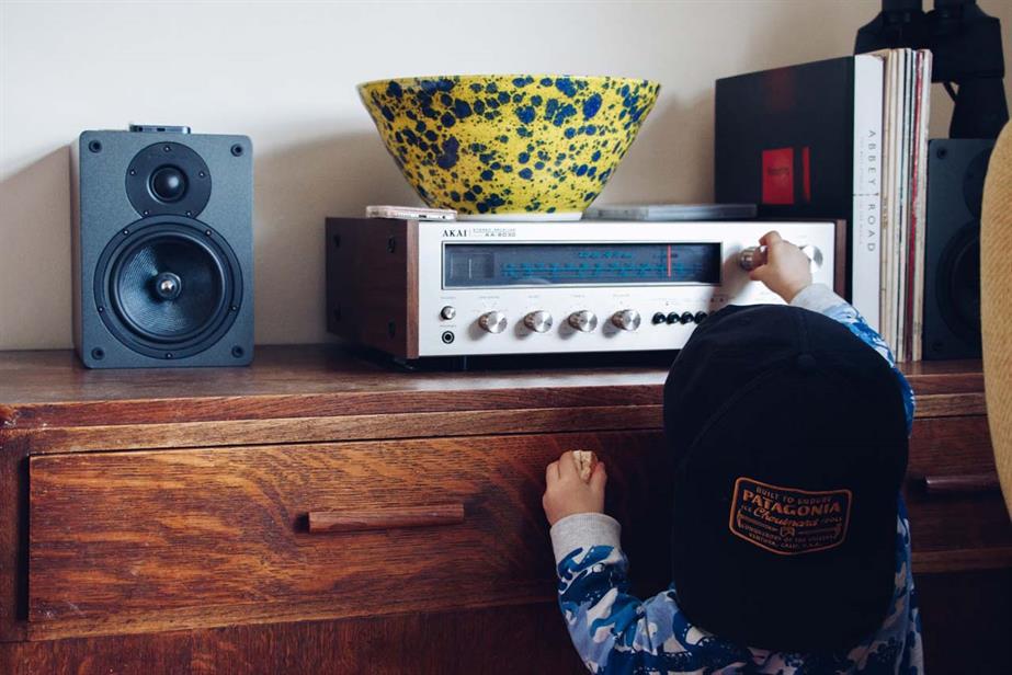 A toddler reaches up to twist the dial of an old radio