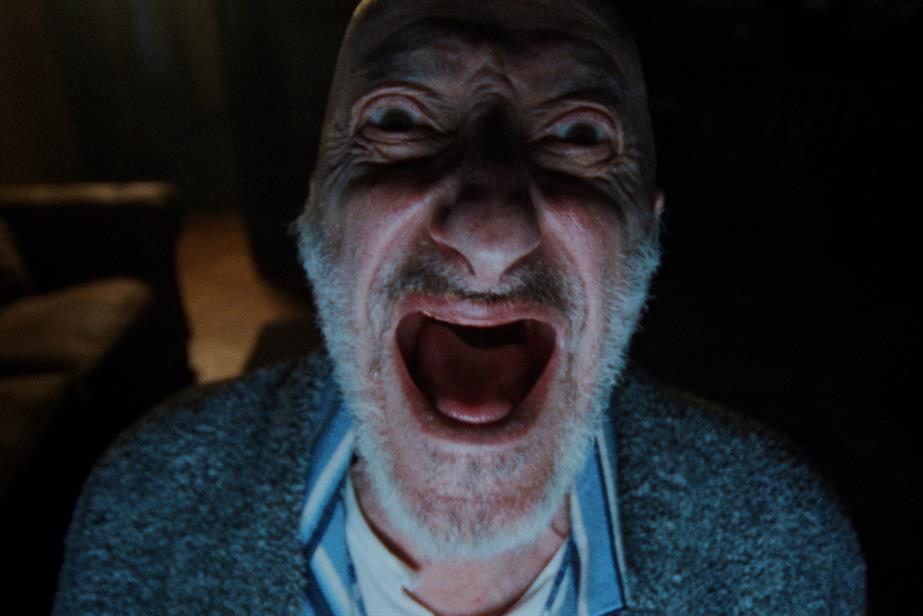 an old man's face in a darkened room screams at the camera