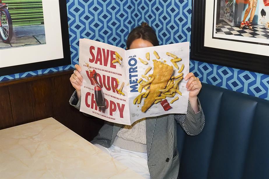 A woman reading a newspaper with cover wrap saying 'save your chippy'