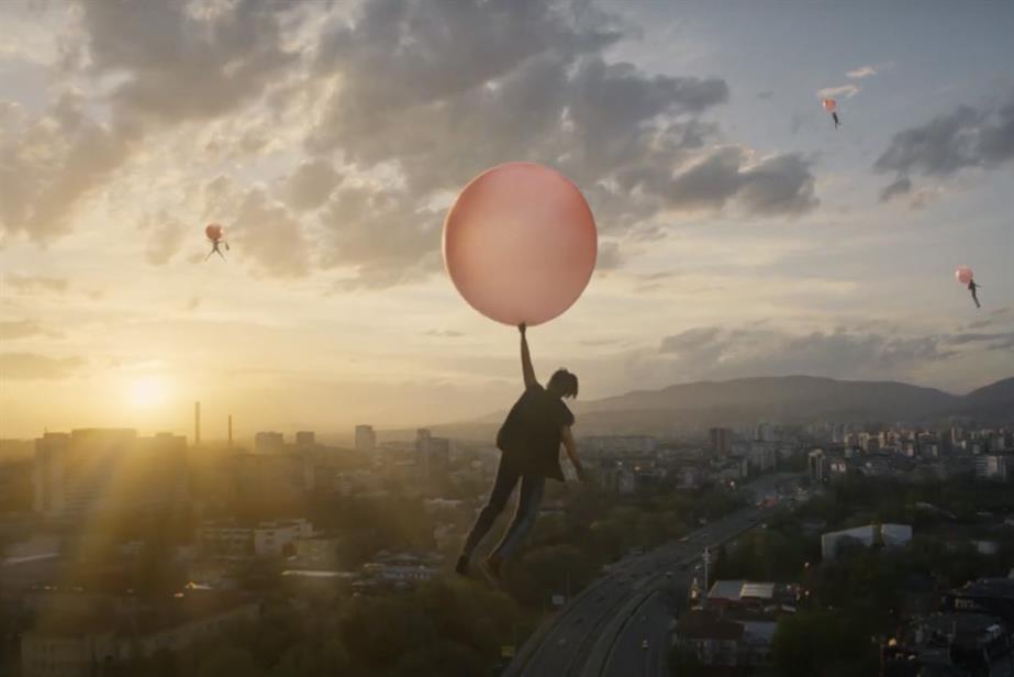 People holding red balloons and flying over a city
