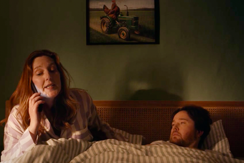 A woman, in bed with her partner, answers her phone