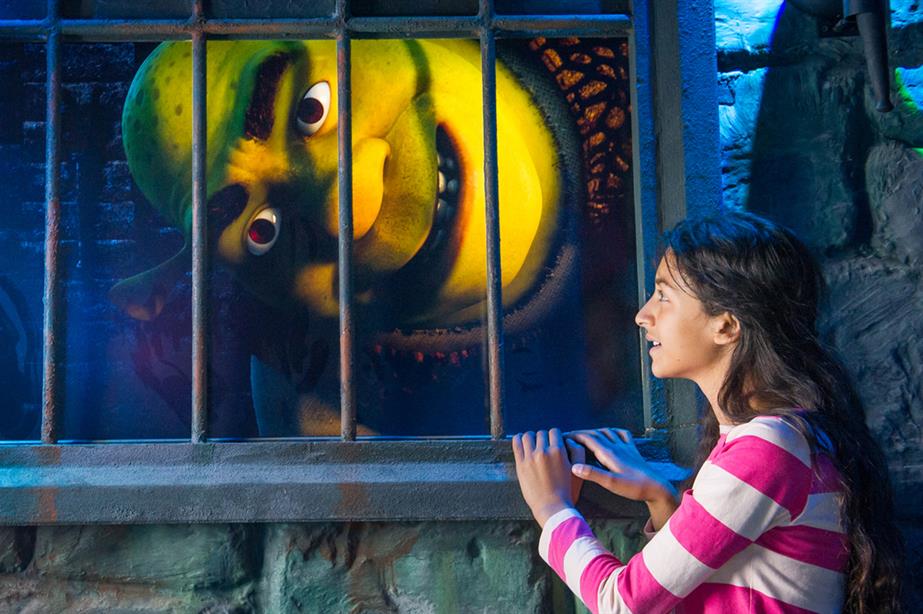 A girl stares at a giant Shrek face in a window at the London attraction Shrek's Adventure!