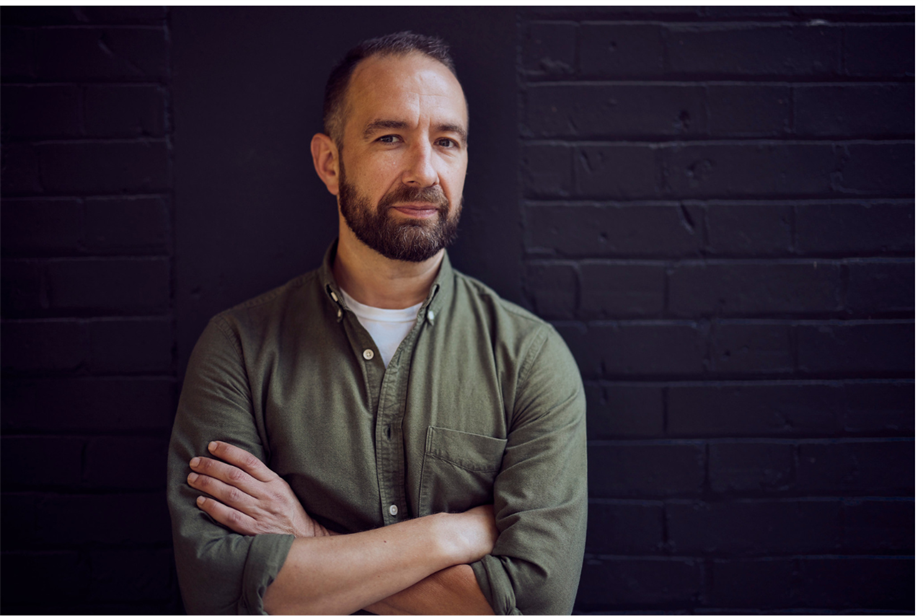 Robin Clarke photographed with crossed arms against a black wall 