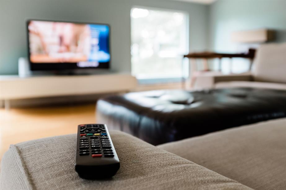 A remote control sitting on a couch with a TV in the background. Photo: Getty Images