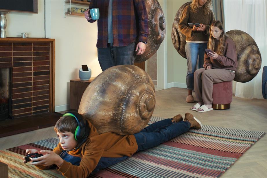 A young boy lies down on his front playing video games with a snail shell on his back.