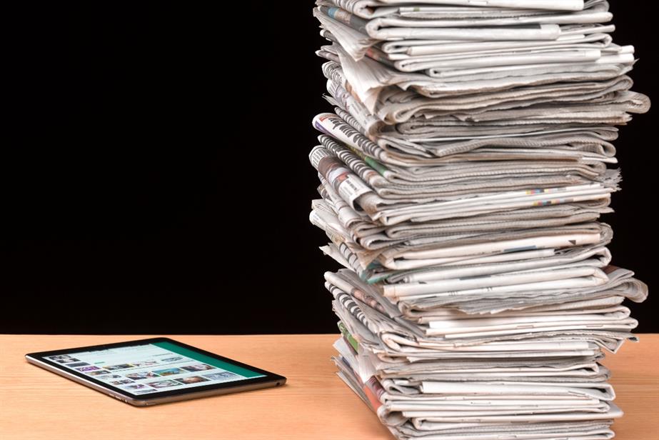 A stack of newspapers next to a tablet.