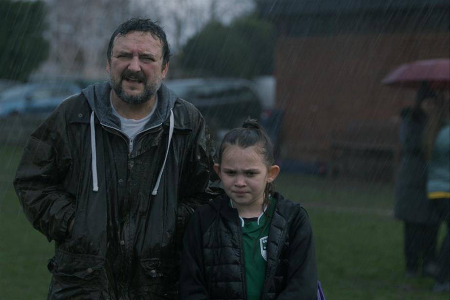 Father and duaghter on football pitch in rain