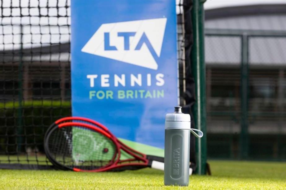 A reusable water bottle and two tennis rackets infront of a poster with the words LTA Tennis for Britain