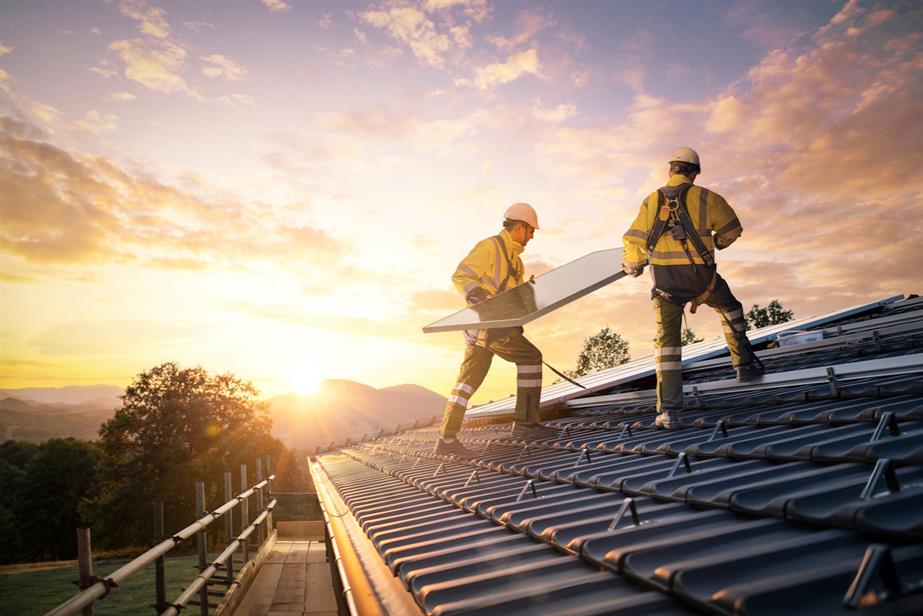 Two men in yellow high-vis install solar panels on a roof