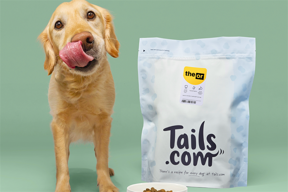 A dog standing next to a bowl and a bag of food from Tails.com