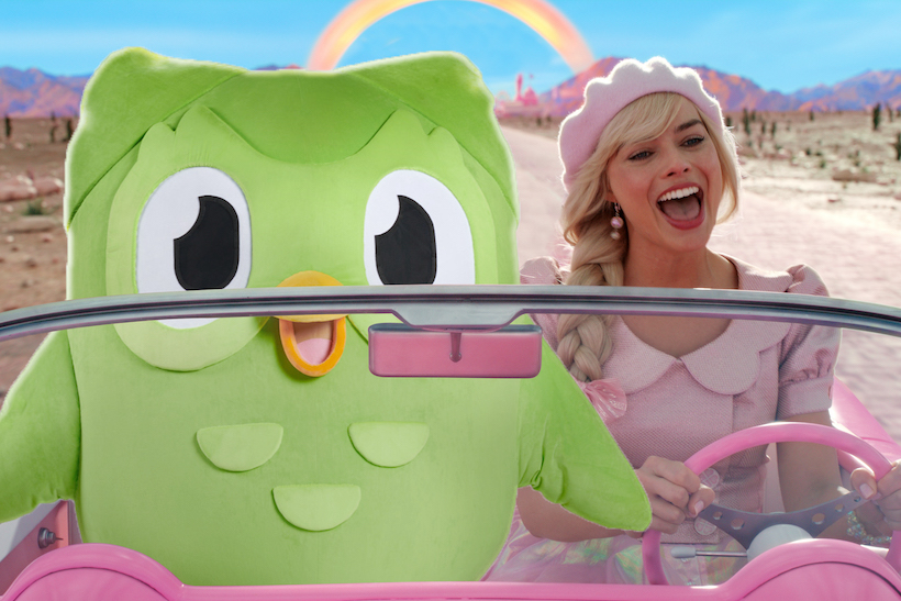 Duolingo mascot owl riding in a car next to Margot Robbie as Barbie 