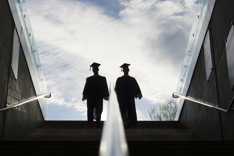 Two figures in college graduation gowns walking down stairs