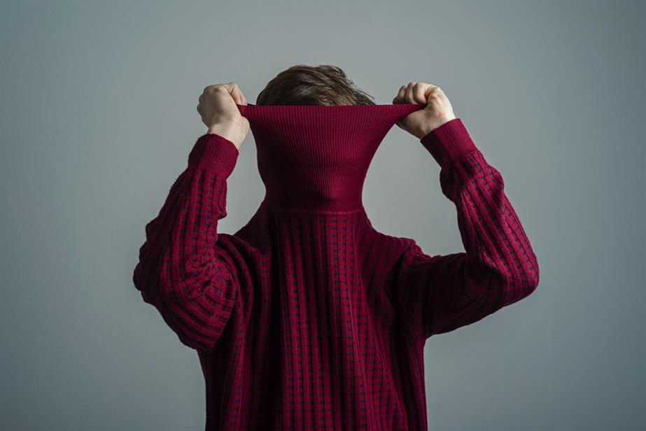 A boy pulls a red sweater over his head