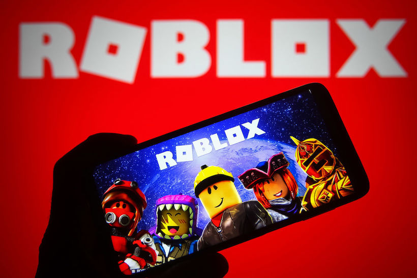Hand holding smart phone displaying Roblox screen